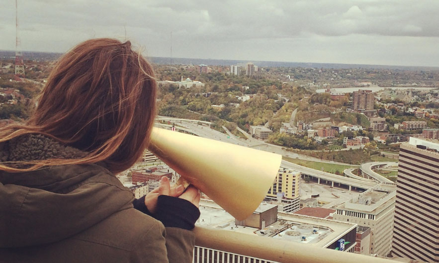 woman holding golden cone to hear the city artwork Corrina Mehiel