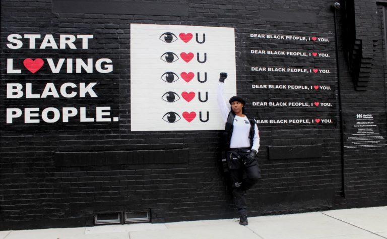 Mary standing in front of black wall with the statements “start loving Black people,” “I love you” and “dear Black people, I love you.”